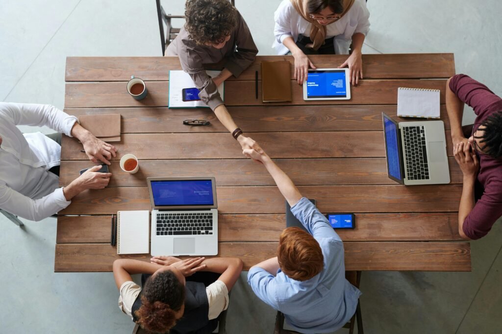 As 30 Perguntas Mais Feitas em Entrevistas de Emprego (Com as Melhores Respostas) Overhead view of colleagues in a work meeting using laptops and tablets, emphasizing teamwork and technology.
