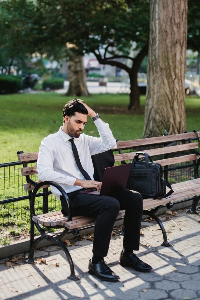 📌 Dicas para quem quer mudar de área profissional (guia completo para fazer a transição com segurança) A businessman working on his laptop on a park bench, suggesting remote work flexibility.
