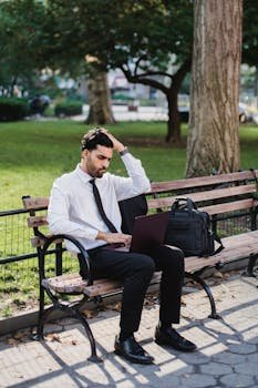 A businessman working on his laptop on a park bench, suggesting remote work flexibility.