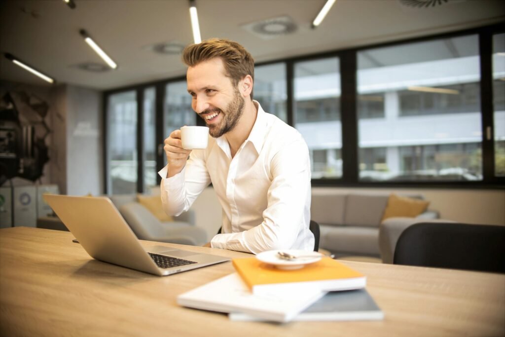 📌 Como usar o LinkedIn para conseguir emprego mais rápido (guia completo com técnicas que funcionam) Man enjoying a coffee break while working in a modern office with laptop and books.