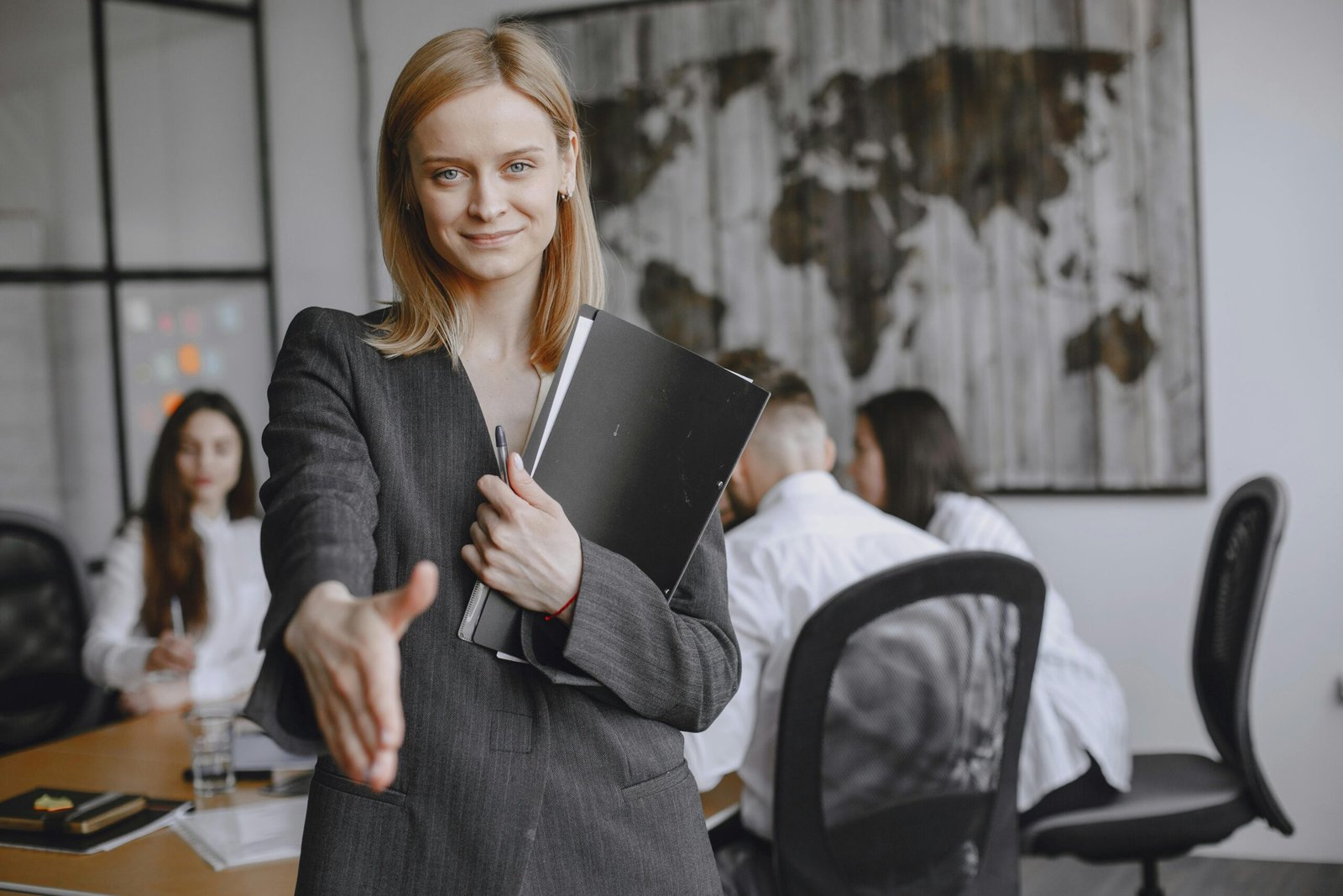 Home Professional woman offering a handshake in a vibrant office setting, symbolizing teamwork and collaboration.