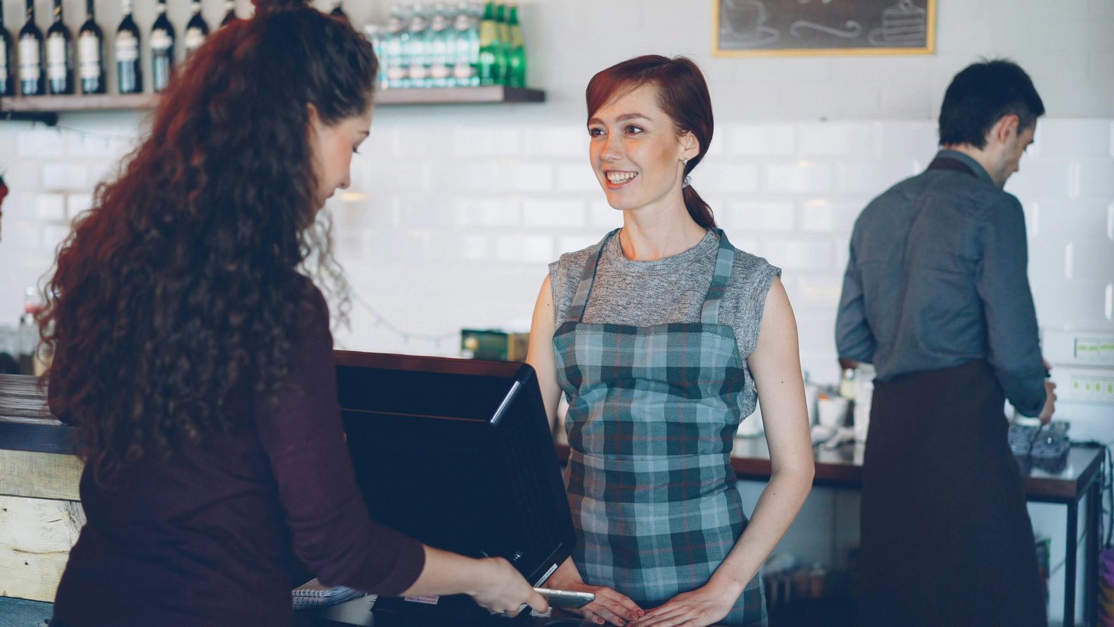 Smiling barista interacting with a customer at the counter in a cozy cafe setting.