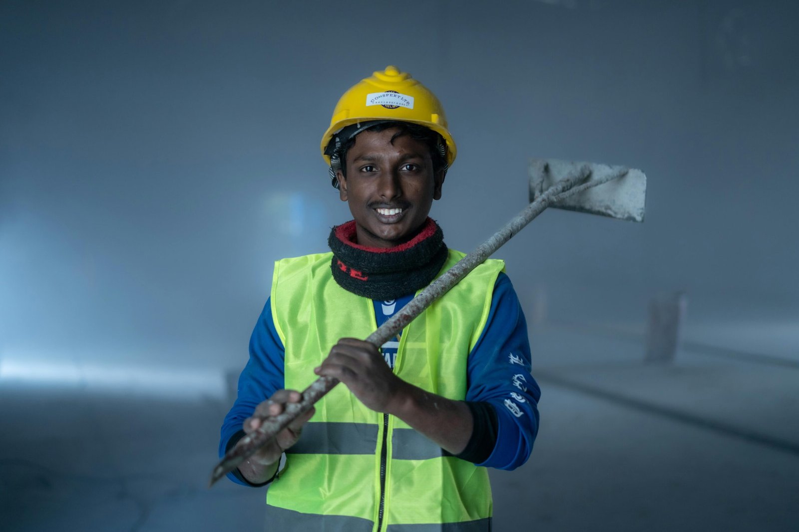 Smiling construction worker in safety gear holds a tool indoors at a work site.