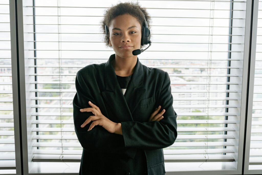 Confident female customer service representative with headset standing by window in office.
