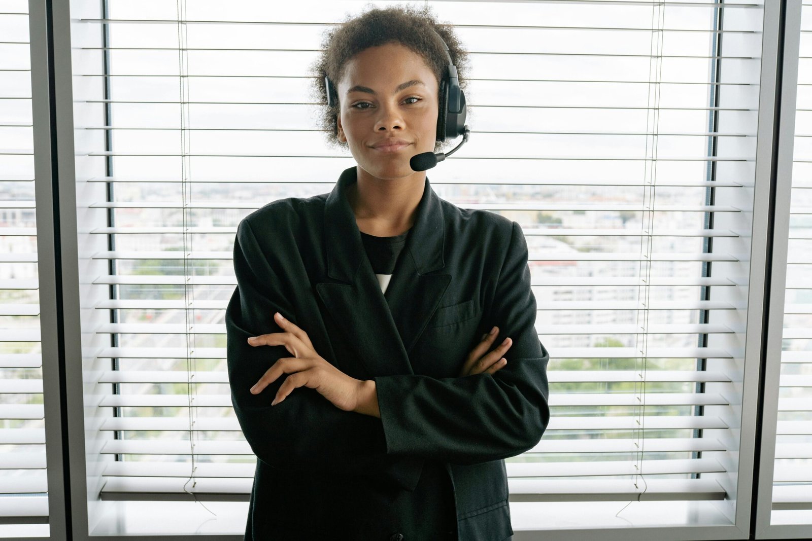 Confident female customer service representative with headset standing by window in office.