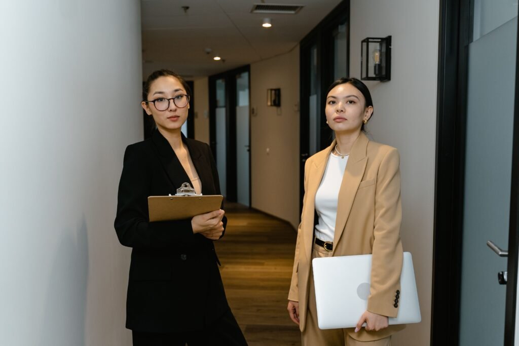 Two businesswomen in suits standing confidently in an office hallway, representing leadership.